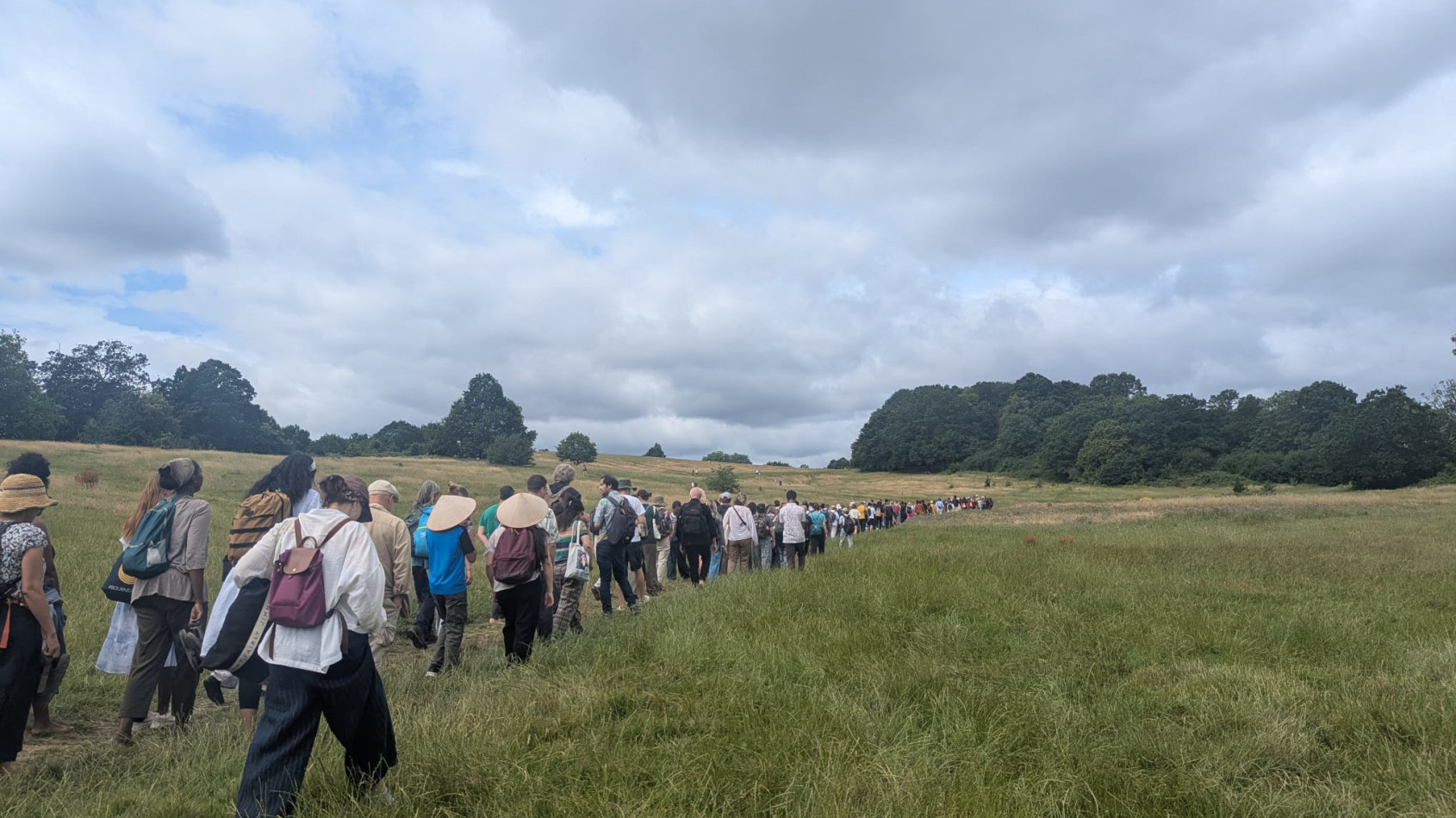 Long line of people walking across fields with trees in the distance